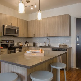 Kitchen with Island Angled View Light-filled Denver apartment kitchen with island, stainless steel appliances, and wood cabinetry.
